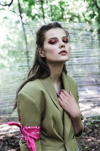 a woman in a green jacket and pink scarf posing in the woods